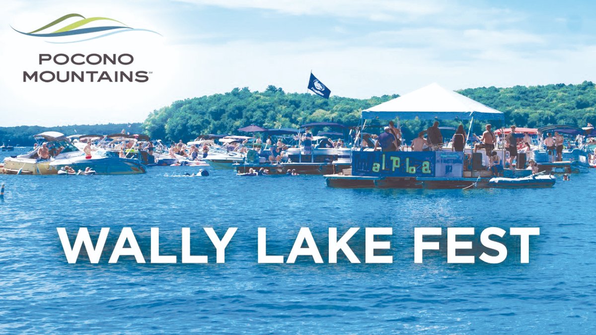 Boats and people gather on a lake under a blue sky during Wally Lake Fest, with a tent on a floating platform.